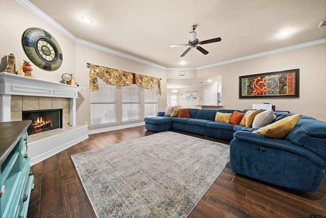 living room featuring dark hardwood / wood-style flooring, a tiled fireplace, ceiling fan, and ornamental molding