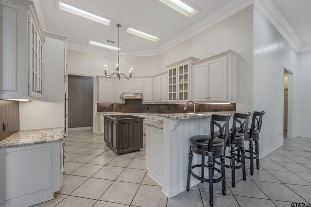 kitchen with light tile patterned floors, crown molding, a breakfast bar area, a center island with sink, and white cabinets