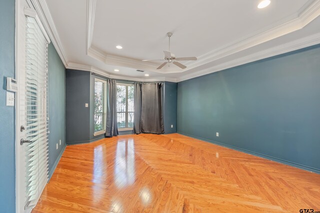 empty room with ceiling fan, a raised ceiling, ornamental molding, and light parquet flooring