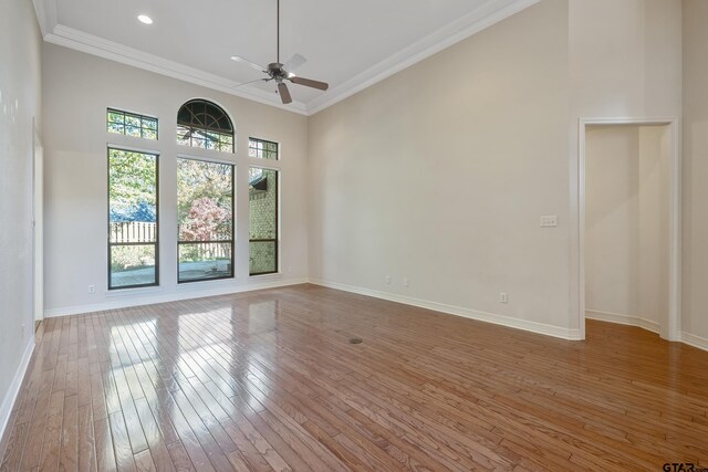 unfurnished room featuring ceiling fan, a towering ceiling, wood-type flooring, and ornamental molding