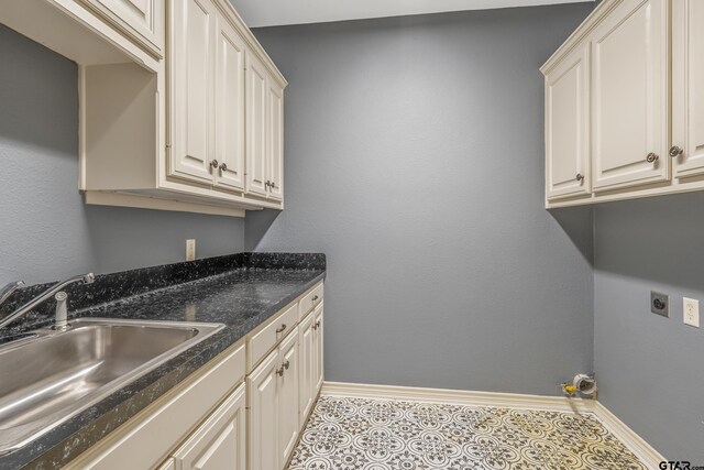 washroom with hookup for an electric dryer, light tile patterned floors, cabinets, and sink