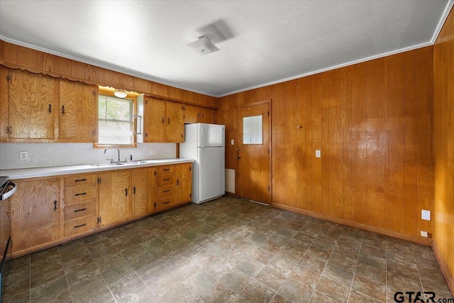 kitchen with a sink, wood walls, freestanding refrigerator, and light countertops