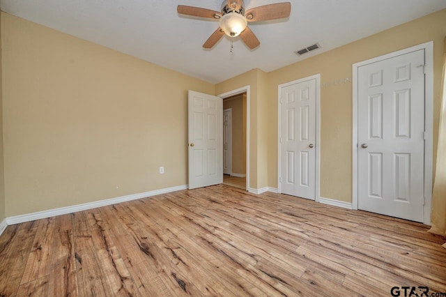 unfurnished bedroom with ceiling fan, two closets, and light wood-type flooring