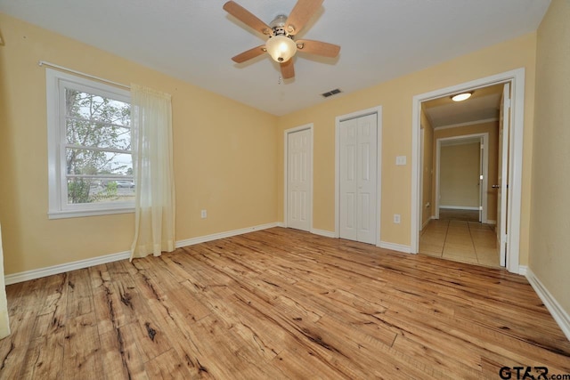 unfurnished bedroom with ornamental molding, light hardwood / wood-style flooring, ceiling fan, and multiple closets