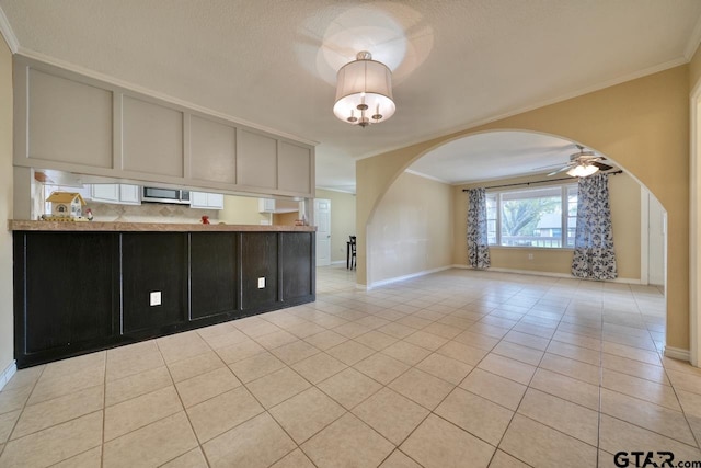 kitchen with ceiling fan with notable chandelier, ornamental molding, kitchen peninsula, and light tile patterned floors