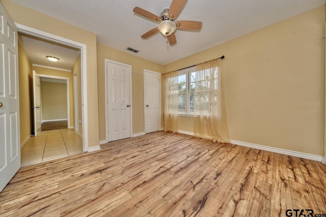 unfurnished bedroom featuring ornamental molding, light hardwood / wood-style flooring, ceiling fan, and multiple closets