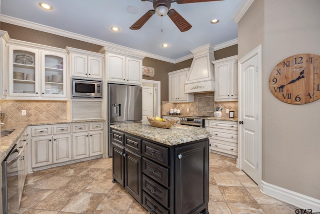 kitchen featuring premium range hood, tasteful backsplash, crown molding, appliances with stainless steel finishes, and a kitchen island