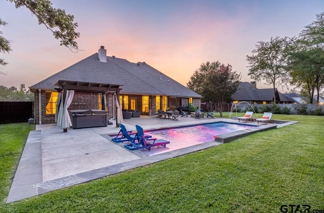 pool at dusk with pool water feature, a hot tub, a patio area, and a lawn