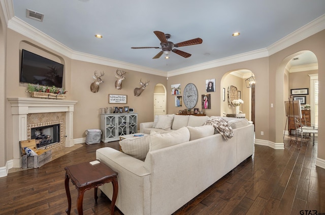 living room featuring a tiled fireplace, ornamental molding, dark hardwood / wood-style floors, and ceiling fan