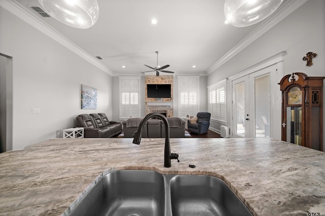 kitchen with light stone countertops, ornamental molding, a stone fireplace, and sink