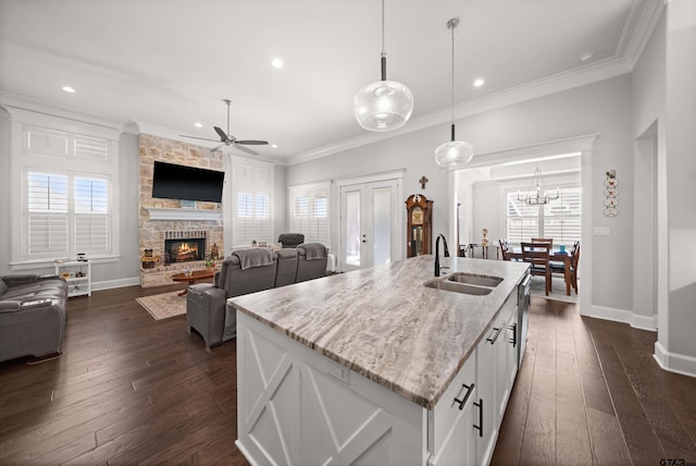 kitchen featuring a stone fireplace, sink, pendant lighting, a kitchen island with sink, and white cabinets