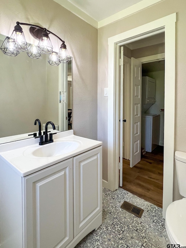 bathroom featuring toilet, stacked washing maching and dryer, vanity, and hardwood / wood-style flooring