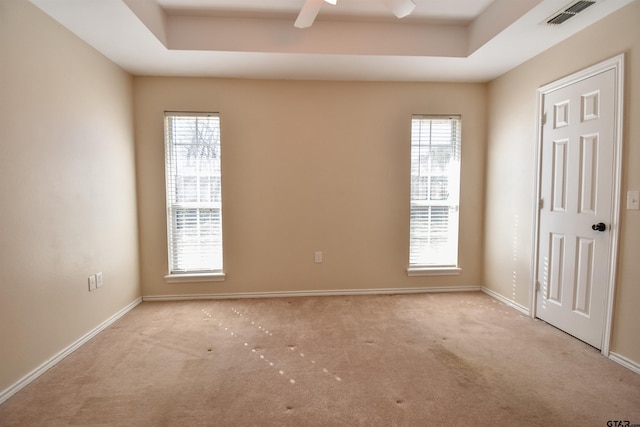 empty room with light carpet, a raised ceiling, and ceiling fan