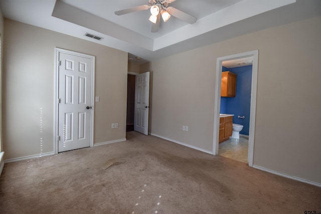 unfurnished bedroom with light carpet, connected bathroom, a tray ceiling, and ceiling fan