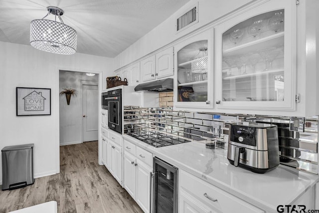 kitchen featuring white cabinets, black appliances, hanging light fixtures, wine cooler, and light hardwood / wood-style floors