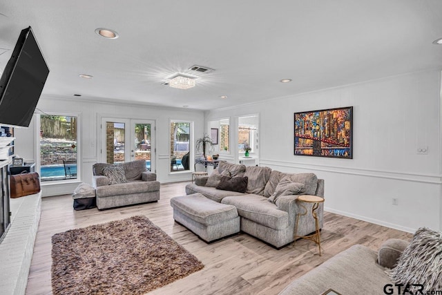 living room with crown molding, plenty of natural light, french doors, and light wood-type flooring