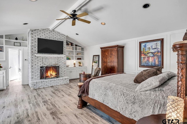 bedroom with ceiling fan, lofted ceiling with beams, a fireplace, and light hardwood / wood-style flooring