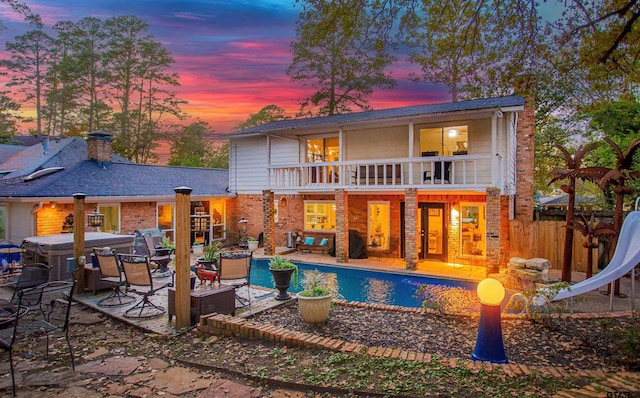 back house at dusk featuring an outdoor living space, a balcony, and a patio