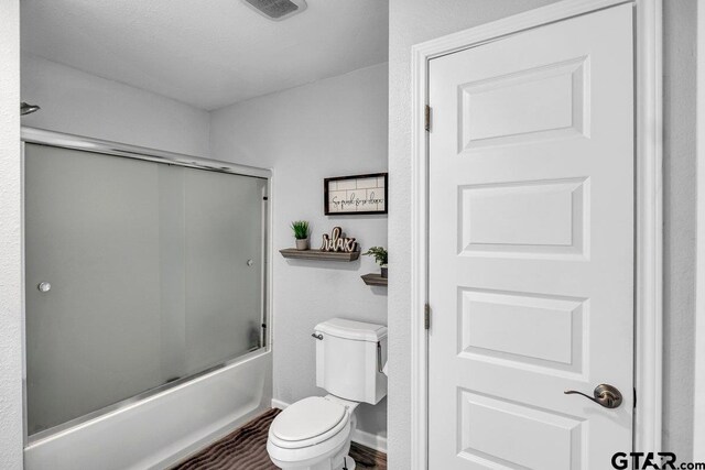 bathroom with toilet and shower / bath combination with glass door