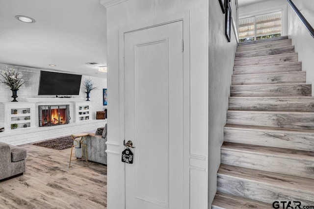 stairs with a fireplace, built in shelves, and hardwood / wood-style flooring