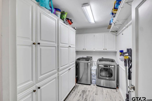 washroom featuring separate washer and dryer, cabinets, a textured ceiling, and light wood-type flooring