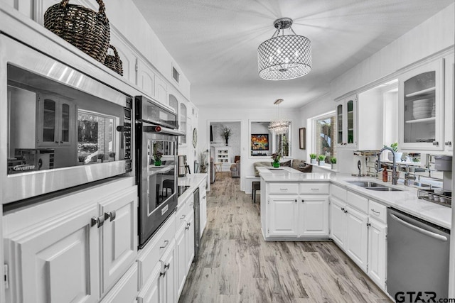 kitchen featuring dishwasher, sink, a chandelier, pendant lighting, and white cabinets