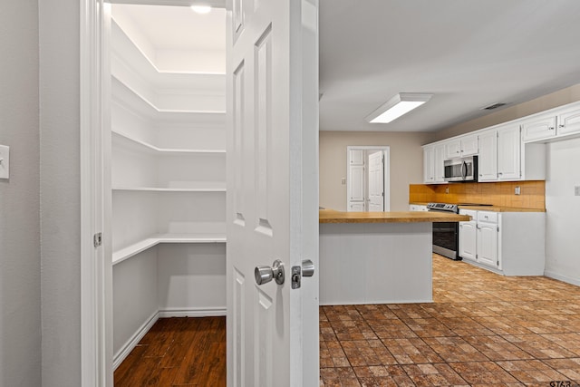 kitchen featuring kitchen peninsula, appliances with stainless steel finishes, white cabinets, and tasteful backsplash