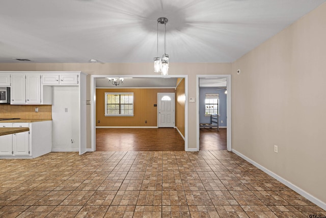 kitchen with ceiling fan with notable chandelier, pendant lighting, white cabinetry, and backsplash