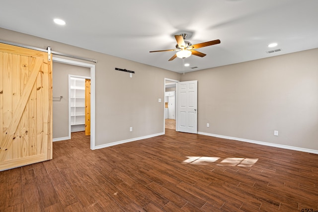 unfurnished bedroom with a spacious closet, hardwood / wood-style flooring, ceiling fan, and a barn door