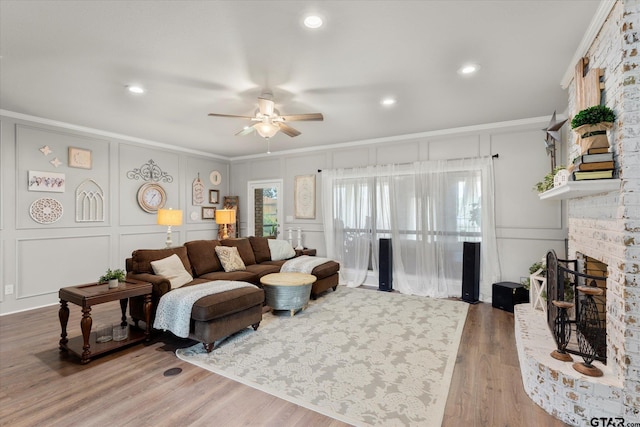 living room with a brick fireplace, wood-type flooring, ornamental molding, and ceiling fan