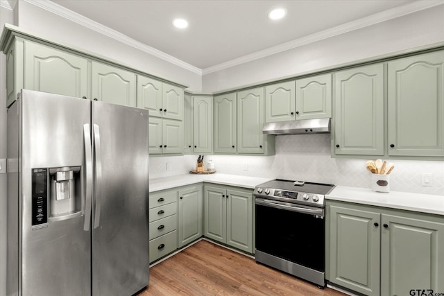 kitchen featuring stainless steel appliances, tasteful backsplash, ornamental molding, green cabinetry, and light hardwood / wood-style flooring