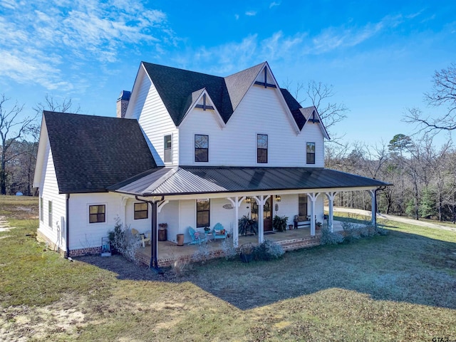 view of front of home with a patio area, a front yard, metal roof, a shingled roof, and a chimney