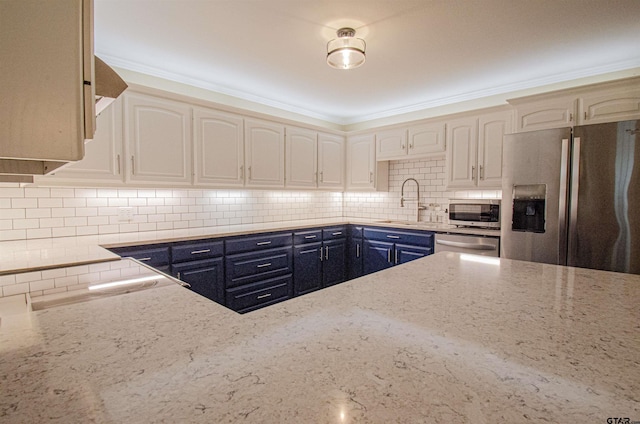 kitchen with a sink, light stone countertops, blue cabinets, appliances with stainless steel finishes, and decorative backsplash