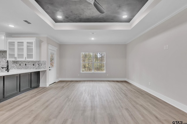 kitchen with a tray ceiling, backsplash, crown molding, and white cabinets