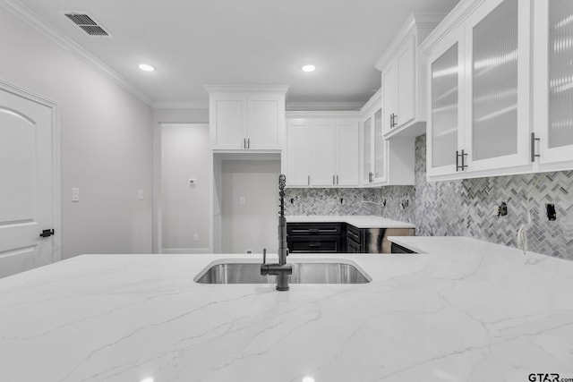 kitchen featuring light stone countertops, decorative backsplash, ornamental molding, sink, and white cabinetry