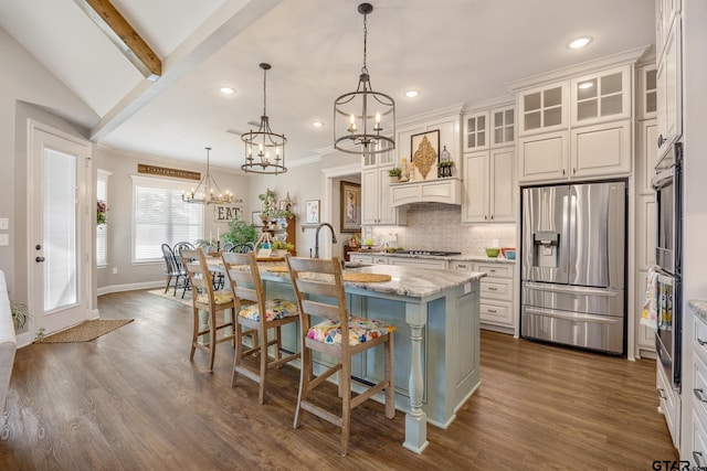 kitchen with light stone countertops, hanging light fixtures, a kitchen island with sink, and stainless steel refrigerator with ice dispenser