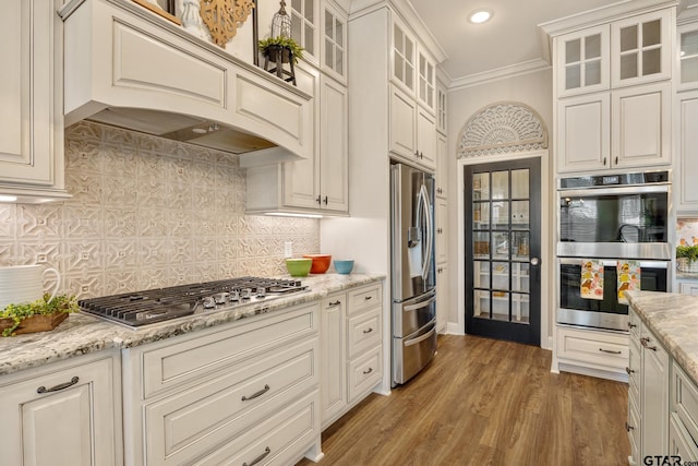 kitchen featuring light stone counters, premium range hood, stainless steel appliances, tasteful backsplash, and crown molding