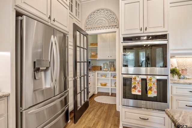 kitchen with light stone countertops, light wood-type flooring, appliances with stainless steel finishes, and white cabinets