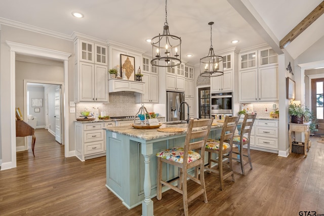 kitchen with a kitchen breakfast bar, an island with sink, hanging light fixtures, lofted ceiling with beams, and appliances with stainless steel finishes