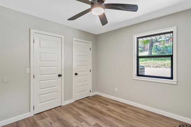 unfurnished bedroom with light wood-type flooring, ceiling fan, and multiple closets