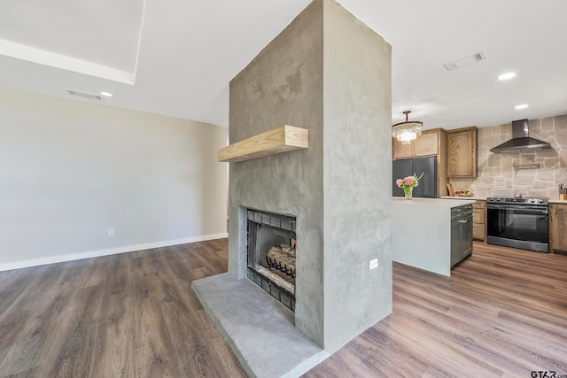 kitchen featuring wall chimney exhaust hood, black fridge, dark hardwood / wood-style flooring, a fireplace, and stainless steel range with electric cooktop