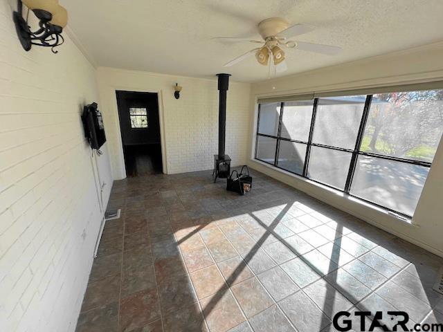 unfurnished sunroom featuring ceiling fan and a wood stove