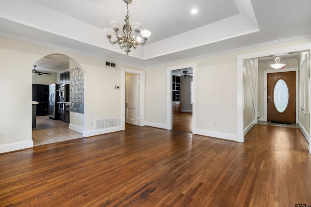 interior space with wood-type flooring, ceiling fan with notable chandelier, and a tray ceiling