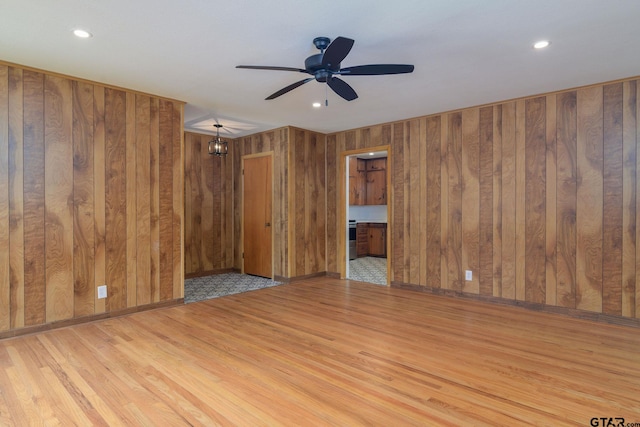 spare room with wood walls, light hardwood / wood-style flooring, and ceiling fan with notable chandelier