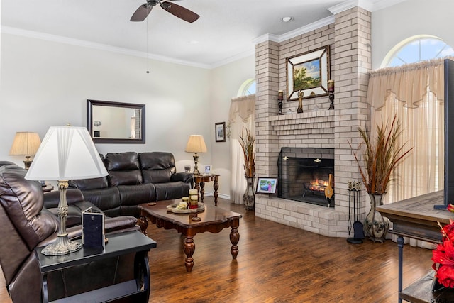 living room featuring a brick fireplace, wood-type flooring, ceiling fan, and crown molding