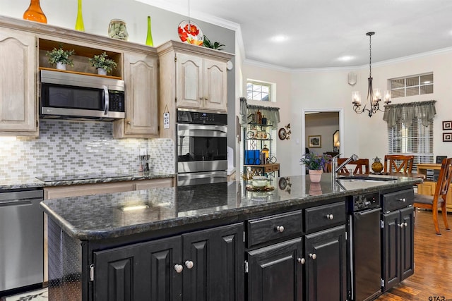 kitchen with ornamental molding, stainless steel appliances, a kitchen island, sink, and dark stone countertops