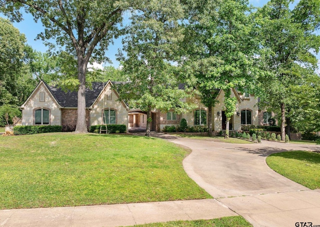 french provincial home featuring a front lawn, curved driveway, and brick siding