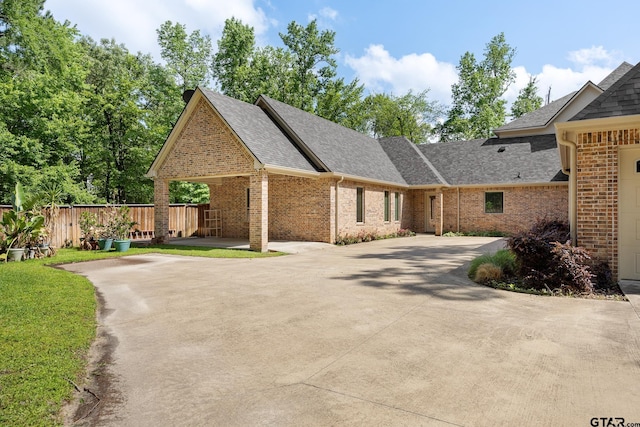 view of front of home with brick siding, roof with shingles, driveway, and fence