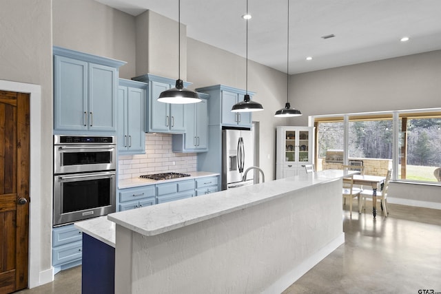 kitchen featuring an island with sink, stainless steel appliances, decorative light fixtures, blue cabinets, and decorative backsplash