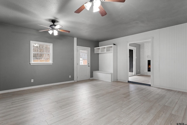 empty room featuring a fireplace, light hardwood / wood-style flooring, a textured ceiling, and ceiling fan